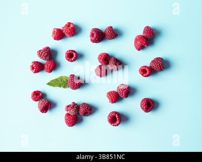 Muster aus reifer roter Himbeere auf blauem Hintergrund. Kreative Gestaltung von Bio-Himbeeren und grünen Blatt. Draufsicht oder flaches Lay. Veganes Essen, Detox Conce Stockfoto