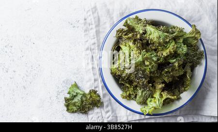 Green Kale Chips mit Salz auf dem Teller. Hausgemachte gesunde Snacks für Low Carb, Keto, kalorienarme Ernährung. Grauer Zementhintergrund. Verzehrfertige Kohl-Chips, Cop Stockfoto