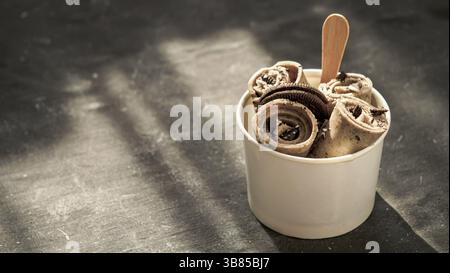 Gerolltes Eis mit in Kegelbecher auf dunklem rustikalem Hintergrund. Eiswürfelrollen mit Keksen Schokolade Sandwich Cookies. Gerolltes Eis im thailändischen Stil mit Polizist Stockfoto