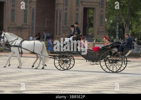 Elegante Pferdekutsche mit Passagieren in Flamenco-Kleidern auf der Plaza de España während der Feria de Sevilla 2025, Sevilla, Andalucía, Spanien. Stockfoto