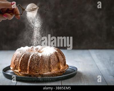 Frau Hand streuen Puderzucker über frische Muffin Kuchen. Puderzucker fällt auf frischen perfekten Muffin-Kuchen. Platz für Text kopieren. Ideen und Rezepte für Stockfoto