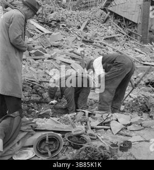 Arbeiter des Zivilschutzes suchen in einem riesigen Schutt- und Holzhaufen nach Überlebenden nach einem verheerenden V1-Angriff in der Highland Road und Lunham Road in Upper Norwood. Ein Feuerwehrmann der Nationalen Feuerwehr bereitet sich darauf vor, Ausrüstung von einem LKW zu heben. Die V-1 und V-2 waren furchterregende Waffen, hatten aber keinen Einfluss auf den Ausgang des Krieges. Die V-1 war eine fliegende Bombe, die fiel, als ihr Treibstoff ausging. Die V2 war eine ballistische Rakete. Beide wurden häufig in westeuropäischen Städten eingesetzt. Stockfoto