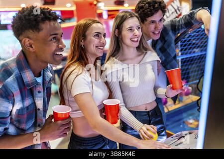 Eine Gruppe glücklicher, multiethnischer Freunde, die ihr Wochenende mit Arcade-Spielen und roten Bechern in einem Unterhaltungslokal genießen Stockfoto