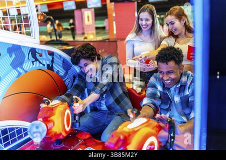 Viele ethnische Freunde verbringen ein Wochenende miteinander, spielen Arkadenbasketball und haben Spaß in einer Bowlingbahn Stockfoto