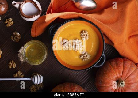 Gebackener Kürbis-Creme-Coup mit Nüssen, Kokosmilch und natürlichem Honig in einer schönen Schüssel serviert. Serviert am braunen Holztisch mit reifem orangenem Pumkins. Flach l Stockfoto