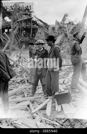 Arbeiter des Zivilschutzes suchen in einem riesigen Schutt- und Holzhaufen nach Überlebenden nach einem verheerenden V1-Angriff in der Highland Road und Lunham Road in Upper Norwood. Ein Feuerwehrmann der Nationalen Feuerwehr bereitet sich darauf vor, Ausrüstung von einem LKW zu heben. Die V-1 und V-2 waren furchterregende Waffen, hatten aber keinen Einfluss auf den Ausgang des Krieges. Die V-1 war eine fliegende Bombe, die fiel, als ihr Treibstoff ausging. Die V2 war eine ballistische Rakete. Beide wurden häufig in westeuropäischen Städten eingesetzt. Stockfoto