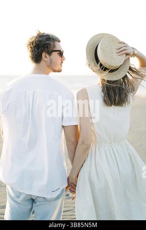 Eine Frau, die einen Strohhut mit der Hand hält, während sie Hand in Hand mit einem Mann steht. Stockfoto