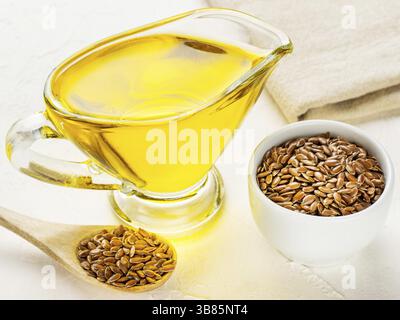 Braune Leinsamen im Löffel und Leinsamenöl in Glaskanne auf trendigem texturiertem weißem Betonhintergrund. Leinöl ist reich an Omega-3-Fettsäuren Stockfoto