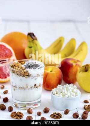 Gesundes Frühstück: Hüttenkäse mit Joghurt, Obst und Nüssen auf weißem Holzhintergrund. Diät, gesundes Lifestyle-Konzept Mahlzeit. Vertikal mit Kopie Stockfoto