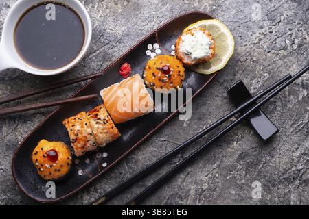 Sushi-Brötchen auf schwarzem Tablett am grauen Tisch. Flache Lagen Stockfoto