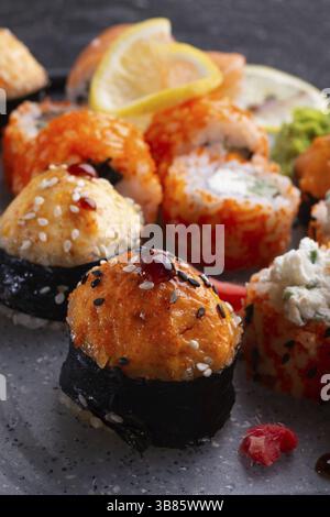 Sushi-Rollenset serviert auf grauem Tablett am schwarzen Tisch. Flach verlegt. Schließen Stockfoto