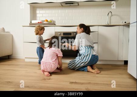 Eine Mutter und ihre beiden Kinder backen fröhlich zusammen in einer modernen Küche. Die Familie bereitet gerne hausgemachte Gerichte zu und fördert die Kreativität Stockfoto