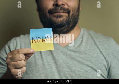 Ein bärtiger Europäer hält einen Aufkleber in Form einer ukrainischen Flagge mit der Aufschrift kein Krieg vor sich Stockfoto
