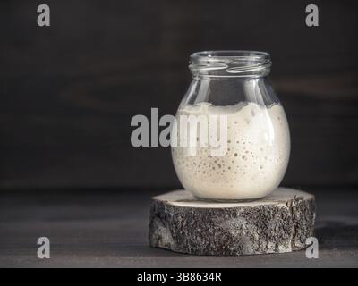 Aktivweizen-Sauerteigstarter im Glasgefäß auf braunem Holzhintergrund. Vorspeise für Sauerteigbrot. Getöntes Bild. Kopierbereich Stockfoto