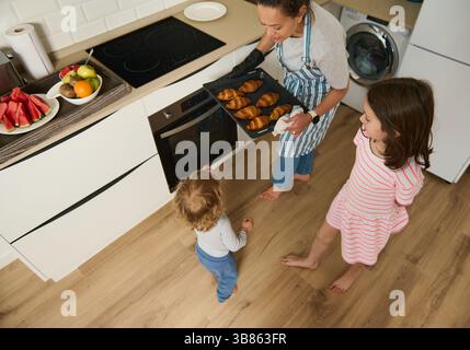 Eine Mutter serviert ihren Kindern in einer modernen Küche frisch gebackene Croissants. Die Atmosphäre ist fröhlich und warm und spiegelt familiäre Bindungsmomente wider Stockfoto