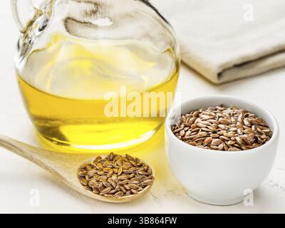 Braune Leinsamen im Löffel und Leinsamenöl in Glasflasche auf trendigem texturiertem weißem Betonhintergrund. Leinöl ist reich an Omega-3-Fettsäuren Stockfoto