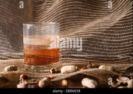 Ein Vintage-Steinglas mit braunem Alkohol auf Sackleinen, Erdnüsse im Vordergrund, Kopierraum rechts Stockfoto
