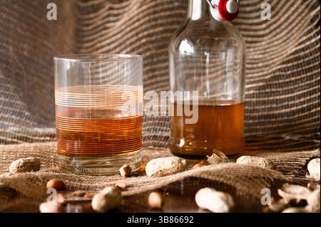 Ein Vintage-Steinglas und eine Flasche brauner Likör und Erdnüsse im Vordergrund Stockfoto