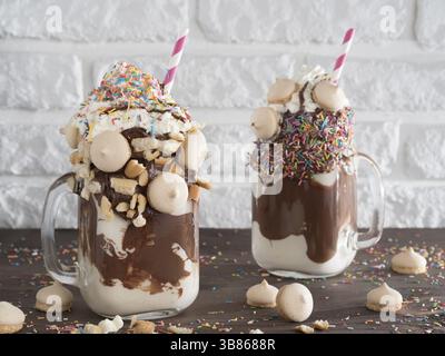 Nahaufnahme von zwei Freakshake im Einmachglas auf braunen Tisch. Ausgeflippt Milchshake mit Schokolade, Keks Kekse und Zucker bestreuen. Trendige Lebensmittel conce Stockfoto
