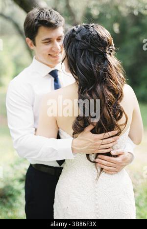 Bräutigam umarmt die Braut mit den Händen auf dem Rücken. Stockfoto