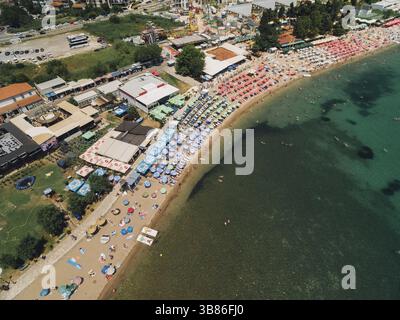 Blick auf den Budva Strand vor der Kulisse von Gebäuden, Grün und Meer. Am Strand gibt es Liegestühle unter Sonnenschirmen. Stockfoto