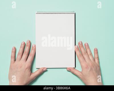 Leeres Notizbuch aus Papier und weibliche Hände. Leeres Papier-Skizzenbuch und Frauenhände auf blauem Hintergrund. Draufsicht oder flache Lagen. Kopierbereich für Text oder Design Stockfoto