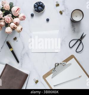 Hochzeit mock up. Wohnung mit leeren Grußkarte legen, Umschlag. Zwischenablage, Blumen, duftende Kerze auf weißem Marmor. Feminine home office Mock up mit Co Stockfoto