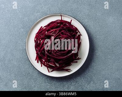 Rohe Rote-Bete-Nudeln von oben. Gemüsenudeln - Rüben-Spaghetti auf Teller über Steingrund. Sauberes Essen, rohes vegetarisches Essenskonzept Stockfoto