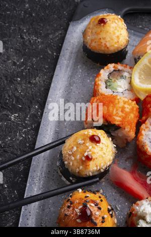 Sushi-Rollenset serviert auf grauem Tablett am schwarzen Tisch. Flach verlegt. Schließen Stockfoto