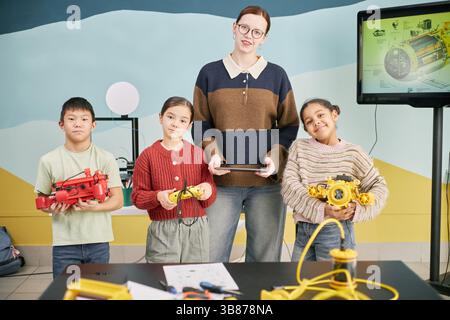 Multiethnische Gruppe von Schülern und Lehrern, die Roboter in einem Klassenzimmer halten, lächeln und sich mit Robotikprojekten beschäftigen, Teamarbeit und cr zeigen Stockfoto