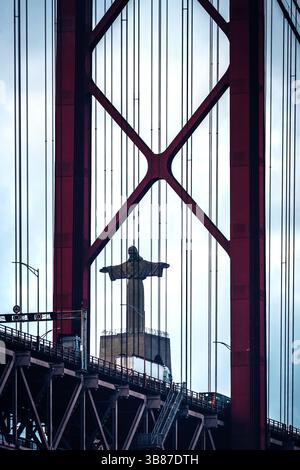 Blick auf die Cristo Rei Statue, eingerahmt von der Brücke vom 25. April in Lissabon, Portugal bei bewölktem Wetter Stockfoto