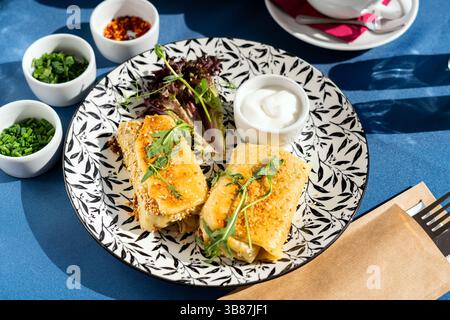Gebratene Sesamkroketten auf Pfannkuchenteig mit griechischem Jogurt. Serviert auf einem weißen Teller. Ein frisches und leckeres Frühstücksset, beleuchtet von der Morgensonne. Stockfoto
