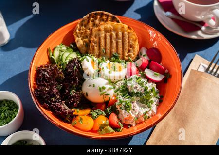 Hartgekochte Eier und weißer Hüttenkäse serviert mit Gemüse, Toast, Kirschtomaten und Gemüse auf einem wunderschönen Orangenteller, ein Frühstücksset Stockfoto