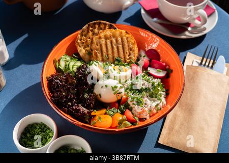 Hartgekochte Eier und weißer Hüttenkäse serviert mit Gemüse, Toast, Kirschtomaten und Gemüse auf einem wunderschönen Orangenteller, ein Frühstücksset Stockfoto