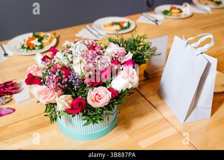 Ein wunderschön gestalteter Strauß aus Rosen und gemischten Blumen in einer dekorativen Box, platziert auf einem festlichen Esstisch, der zum Feiern aufgestellt wird. Stockfoto