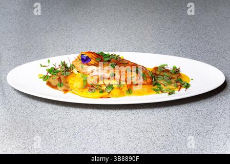 Elegantes, überzogenes Lachsfilet mit Mangohauce, Mikrogrün und einem essbaren Veilchen, ideal für Gourmet-Speisen. Stockfoto