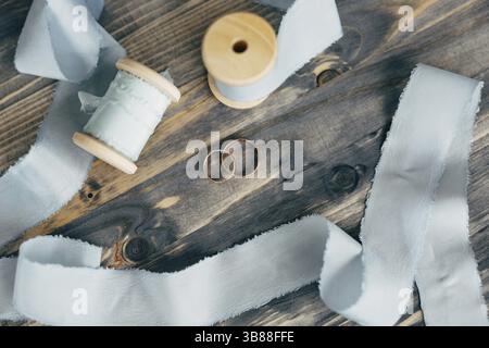Draufsicht auf Hochzeitsringe aus Gold auf einer Holzfläche mit grauen Bandspulen. Stockfoto