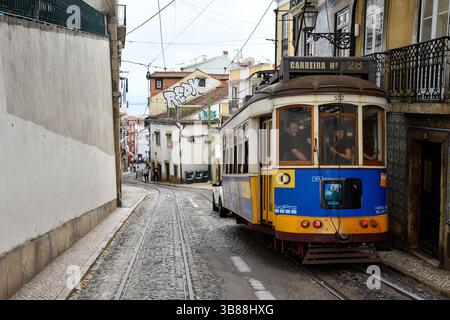 Die berühmte gelbe Straßenbahn 28 führt durch die historischen Straßen von Lissabon, Portugal. Diese alte elektrische Straßenbahn ist eine der beliebtesten Attraktionen der Stadt und bietet eine malerische Aussicht, während sie durch beliebte Viertel wie Graca, Alfama, Baixa und Estrela fährt. Quelle: Duncan Thomas/Majestic Media. Stockfoto