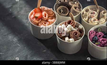 Gerolltes Eis in Kegelbecher auf dunklem Hintergrund. Verschiedene Eisrollen oder Thai Stil gerolltes Eis mit Kopierraum für Text oder Design. Banner. Natu Stockfoto