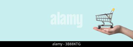 Spielzeug Warenkorb in weiblicher Hand.Einkaufswagen auf Hand über blauem Hintergrund.Kopierraum für Text oder Design.Einkaufswagen nahtloses Muster als Verkauf, di Stockfoto