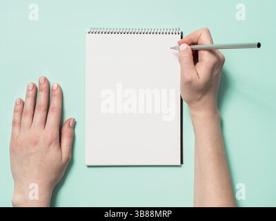 Leeres Papier Notebook und weibliche Hände mit Bleistift. Leere Papier Skizzenbuch mit pincil in Frau Hände auf blauem Hintergrund. Top View oder flach. Kopieren Sie sp Stockfoto
