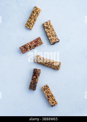 Müsliriegel auf blauem Hintergrund. Set aus verschiedenen Müsliriegeln auf weißem Marmortisch. Oberer Freiheitsgrad Draufsicht oder flache Lagen. Vertikal Stockfoto