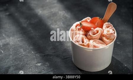 Gerolltes Eis mit Erdbeere in Kegelbecher auf dunklem rustikalem Hintergrund. Banner mit Erdbeereisten Brötchen. Thailändisches Eiscreme mit Kopierplatz für gerolltes Eis Stockfoto