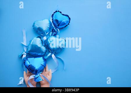 Eine Hand hält blaue, herzförmige Ballons vor einem passenden Hintergrund. Stockfoto