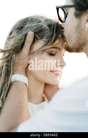 Der Mann küsst Frau auf die Stirn und hält ihren Kopf in den Händen. Hochformat. Stockfoto