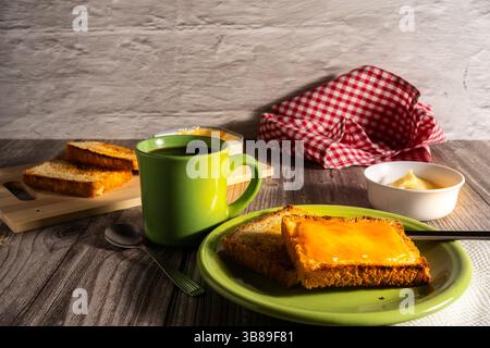 Geröstete Brotscheiben mit Orangenmarmelade und Kaffeetasse auf grünem Teller und rustikalem Holztisch, einfaches Frühstück Stockfoto