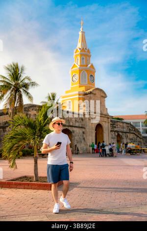Glücklicher junger Lateinreisender in weißem T-Shirt und blauen Shorts, der einen sonnigen Spaziergang am berühmten Uhrenturm in Cartagena, Kolumbien, genießt. Stockfoto