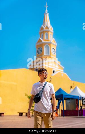Stilvoller junger Latino-Mann in weißem Hemd und khakifarbener Hose lächelt, während er Cartagena, Kolumbien, in der Nähe des berühmten gelben Uhrenturms erkundet. Stockfoto