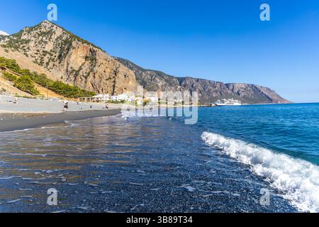 Kreta, Griechenland - 18. Oktober 2024: Blick auf die Küste von Agia Roumeli auf Kreta mit den Klippen der Samaria-Schlucht, die über dem Strand aufragen, und Fähren, die in der Nähe der ankerten Stockfoto