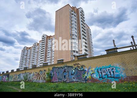 Graffiti auf einem Ziegelzaun und einem mehrstöckigen Wohngebäude am Himmel Stockfoto